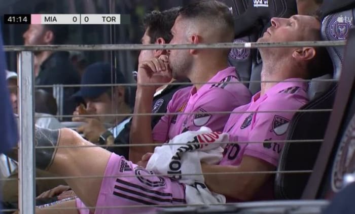 Lionel Messi pictured (right) sat on the Inter Miami bench with his left foot raised after being substituted off during a game against Toronto FC in September 2023